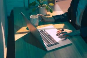 Foto em close das mãos de uma mulher trabalhando em um notebook com uma caneca de café