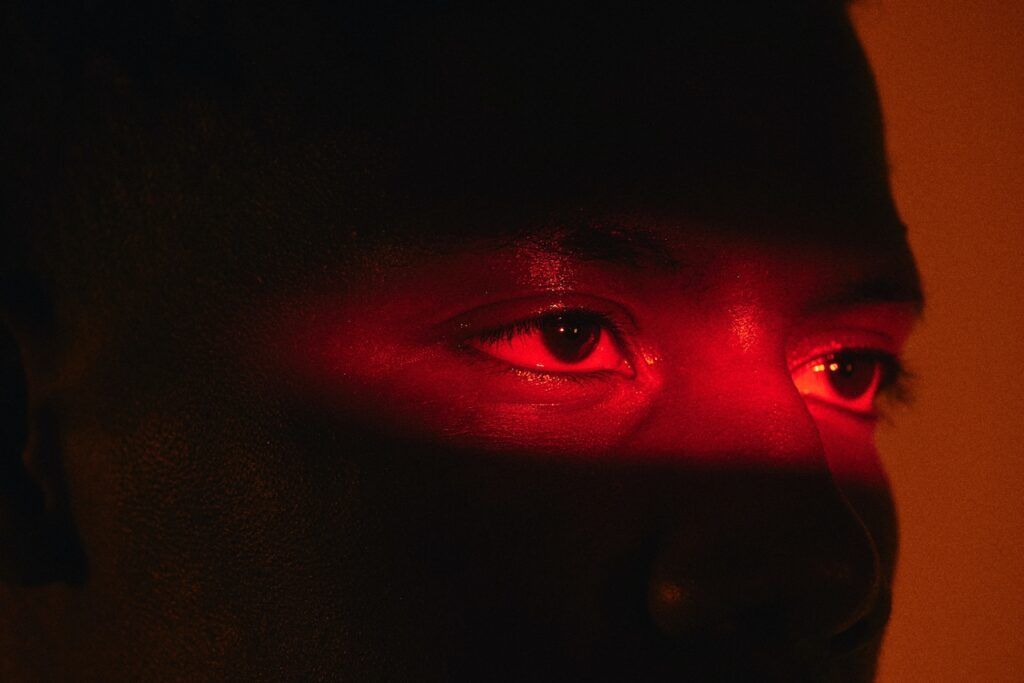 Imagem mostra olhos de uma pessoa negra destacados por uma iluminação vermelha. A foto ilustra pauta sobre racismo algorítmico.