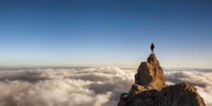 Imagem de um homem no alto de uma montanha, acima das nuvens.